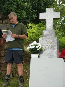 A speaker beside the white memorial cross to Louis Barrau